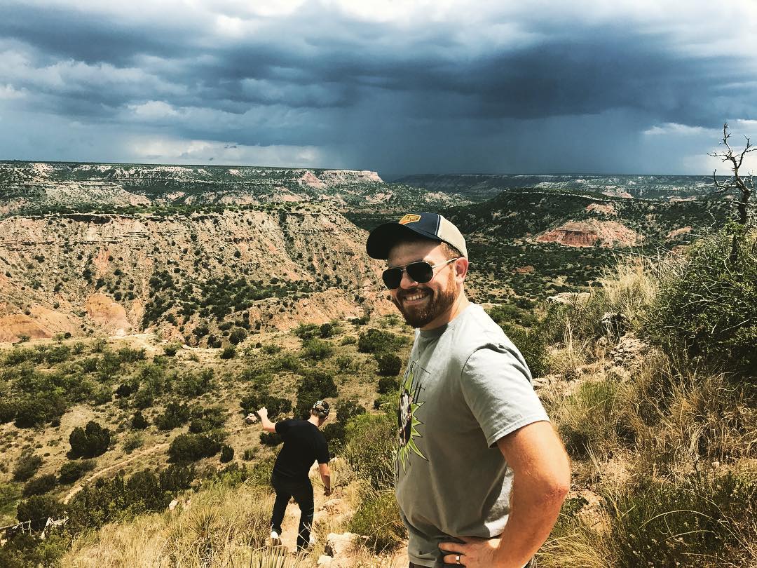 Photo of Will in hat and sunglasses at Palo Duro Canyon State Park with his little brother Drew walking down the hill in the background.