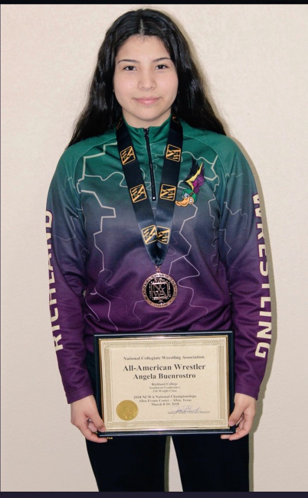 Angelo Buenrostro, All-American Wrestler, recruited to Richland College, holding a certificate, wearing a medal and a jacket with the Thunderduck on it.
